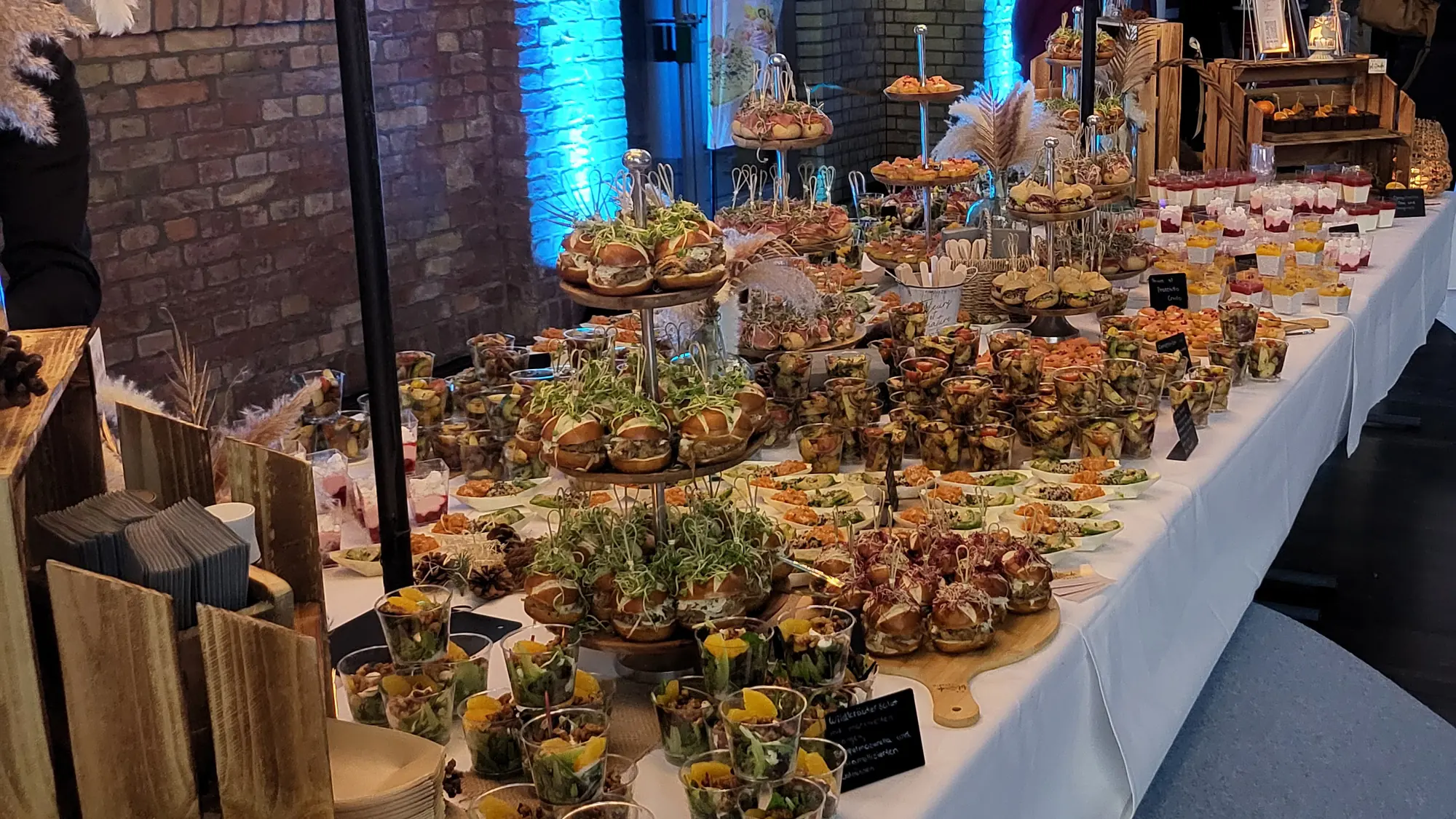 Sehr lange Buffettafel mit hunderten Fingerfood-Portionen unter beleuchteten Blütenbäumen