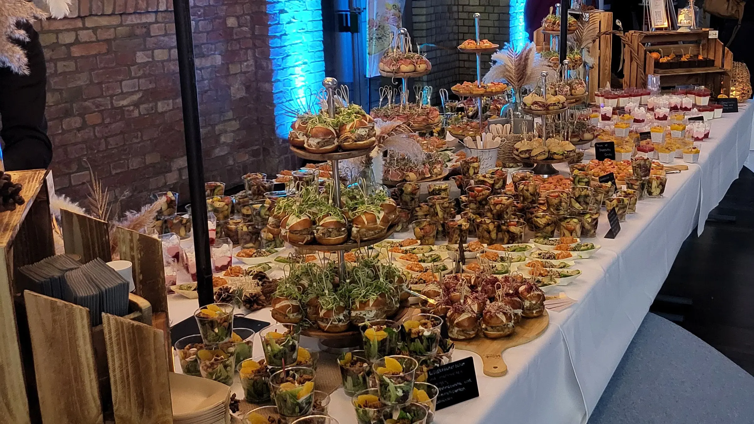 Sehr lange Buffettafel mit hunderten Fingerfood-Portionen unter beleuchteten Blütenbäumen