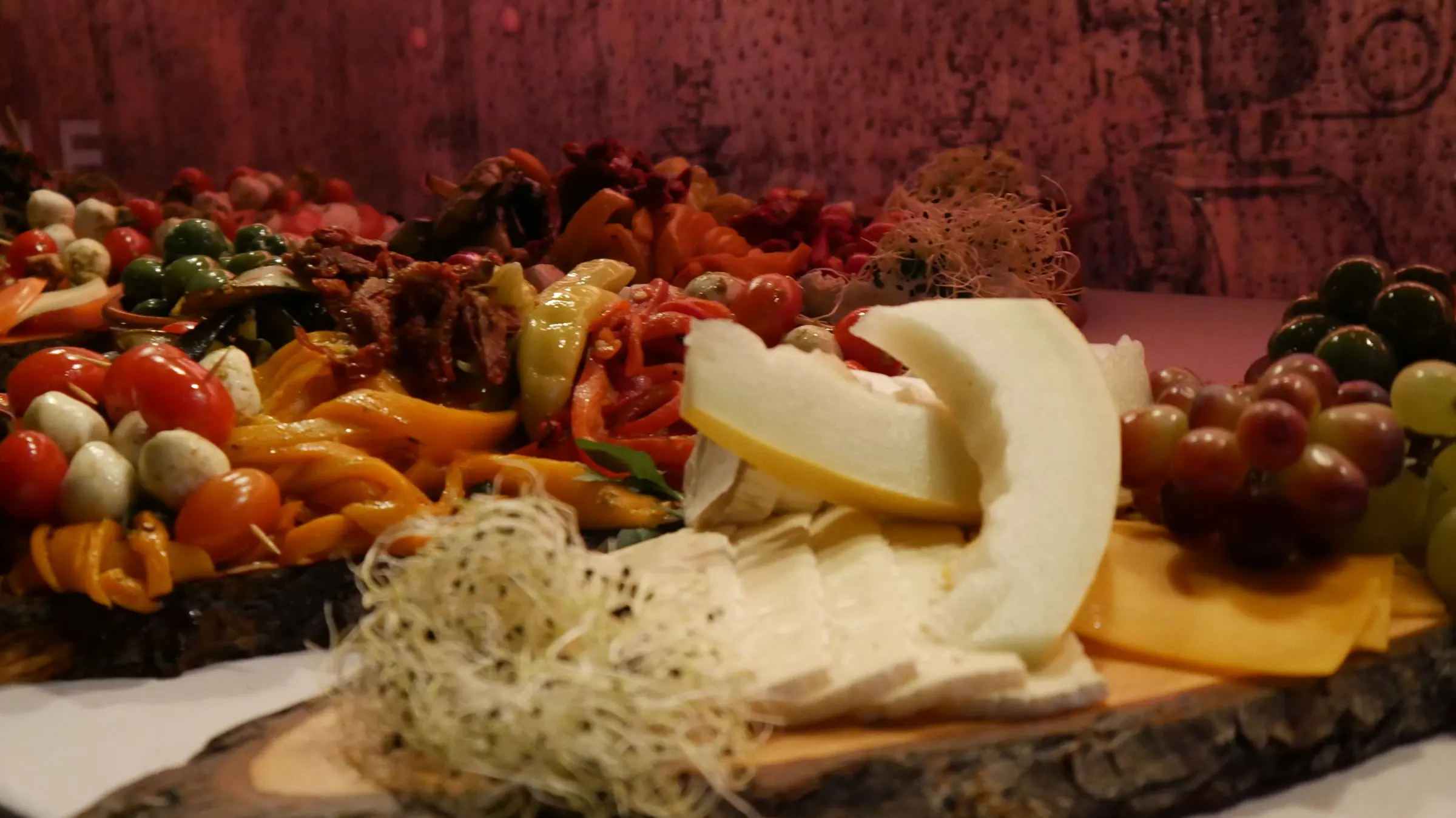 Antipasti-Brett mit Käse, Melone, Oliven und Sprossen auf dunklem Holz