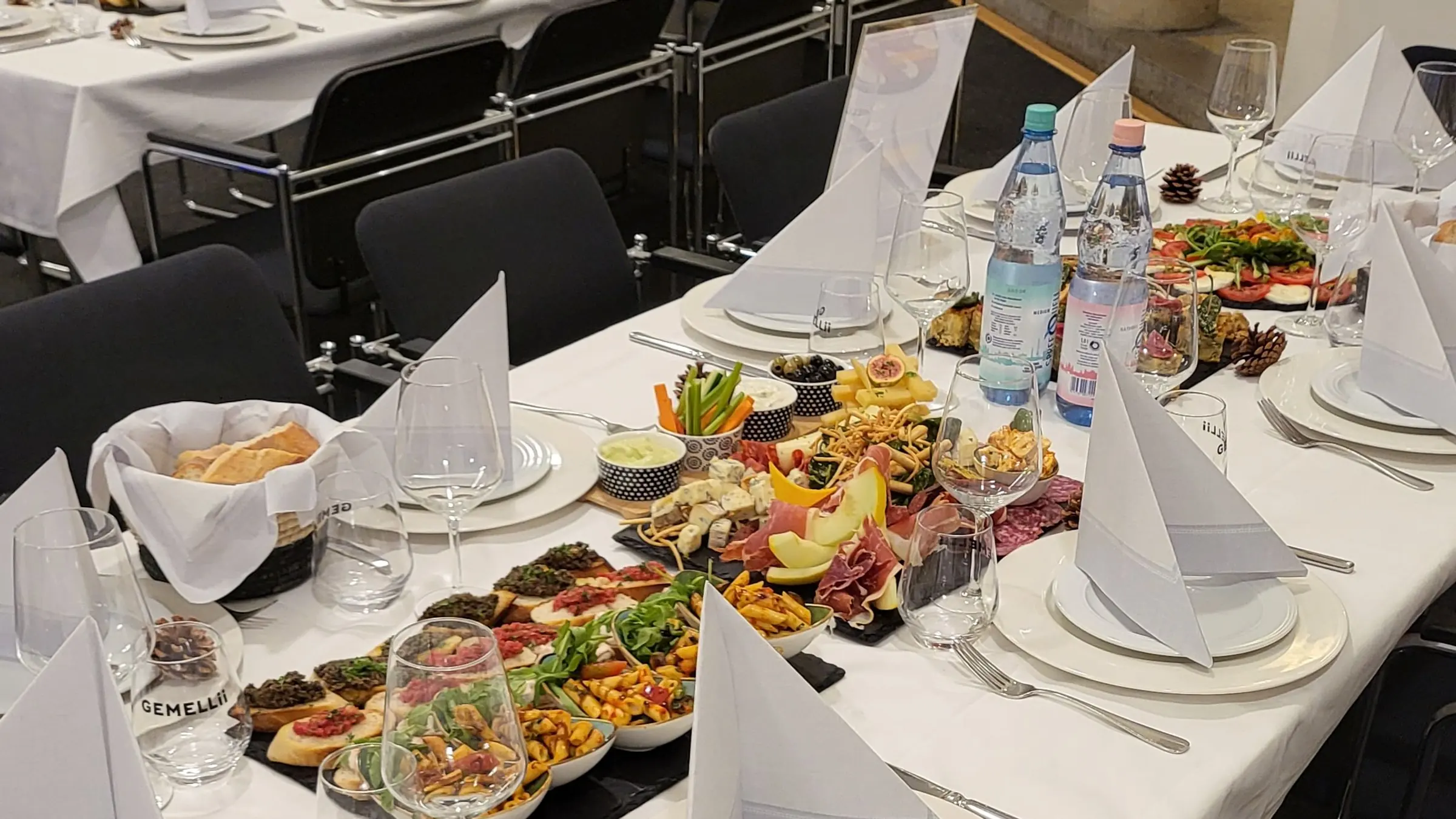 Lange eingedeckte Tafel mit Vorspeisenbrettern, Gläsern und weißen Servietten