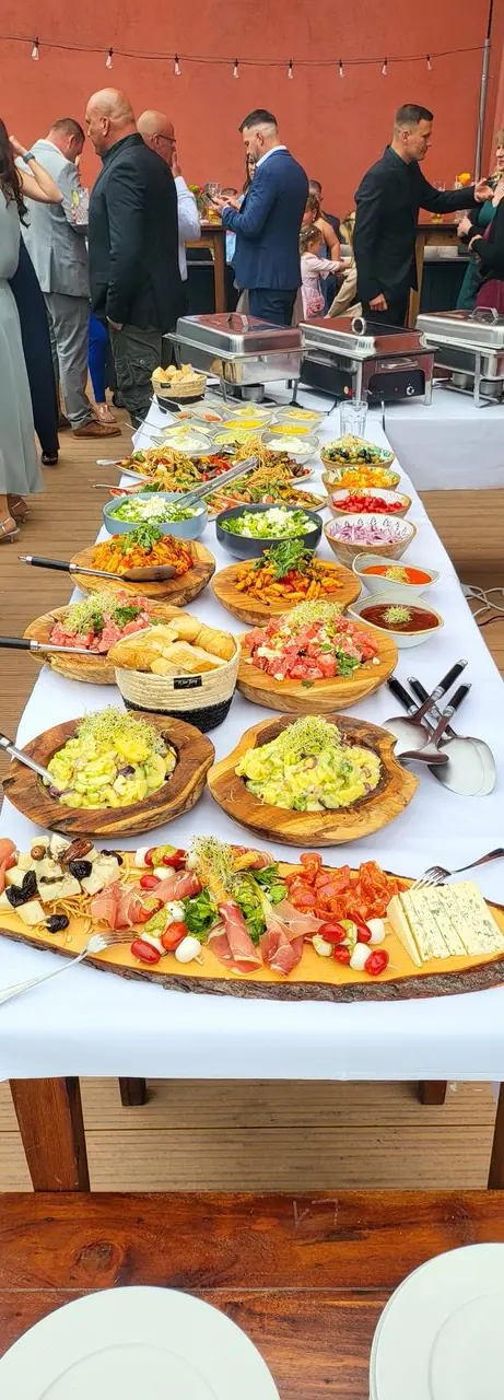 Langes Hochzeitsbuffet im Freien mit Holzbrettern, Salaten und Dips
