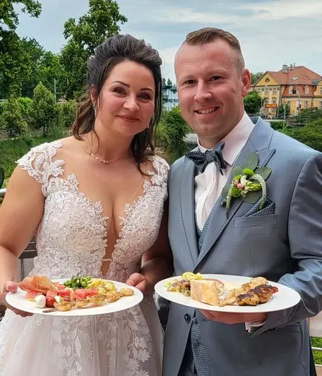 Brautpaar mit Tellern vor einem Hochzeitsbuffet im Freien
