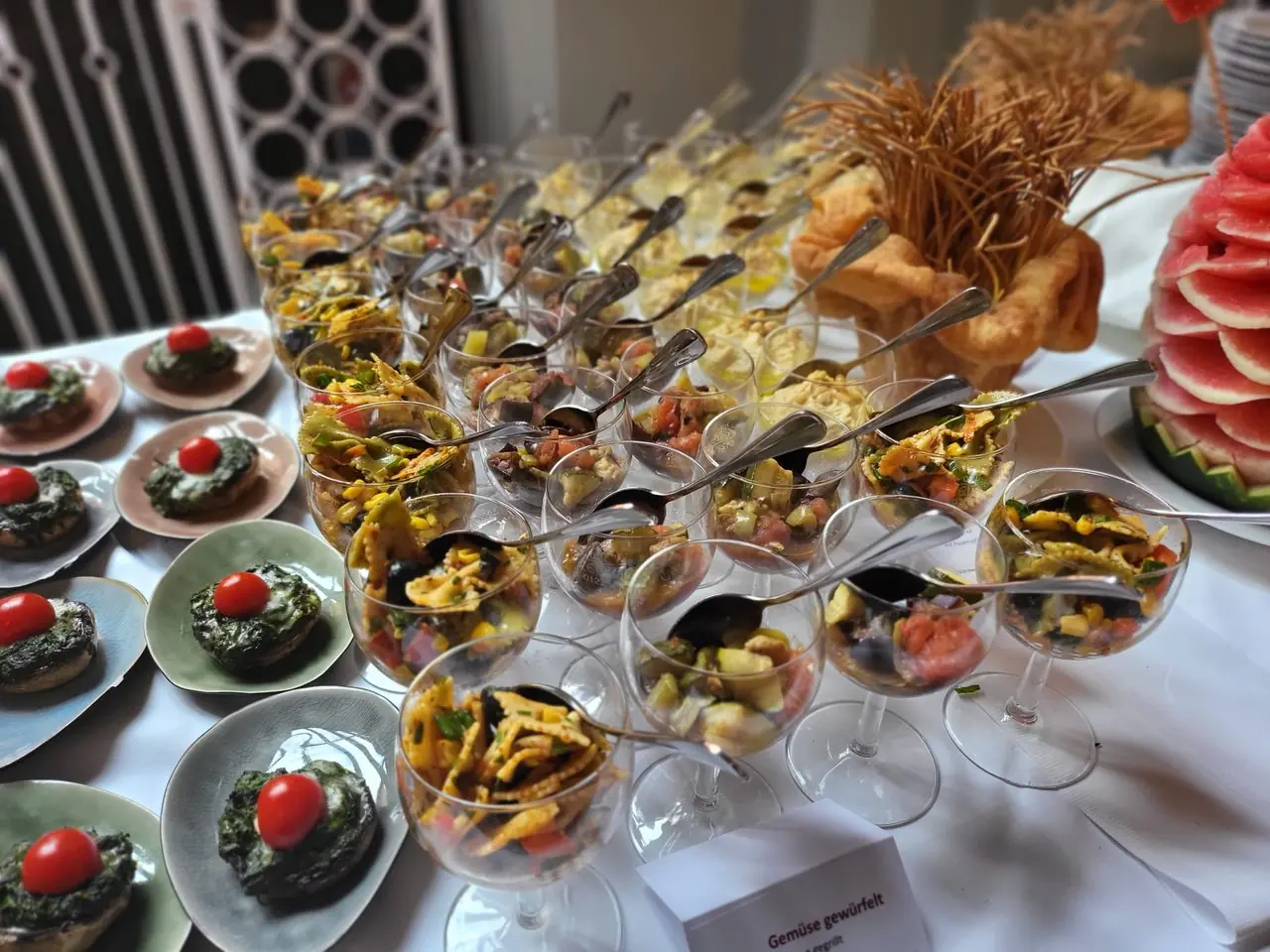Buffet mit Salaten in Stielgläsern, Spinat-Häppchen und geschnitzter Wassermelone