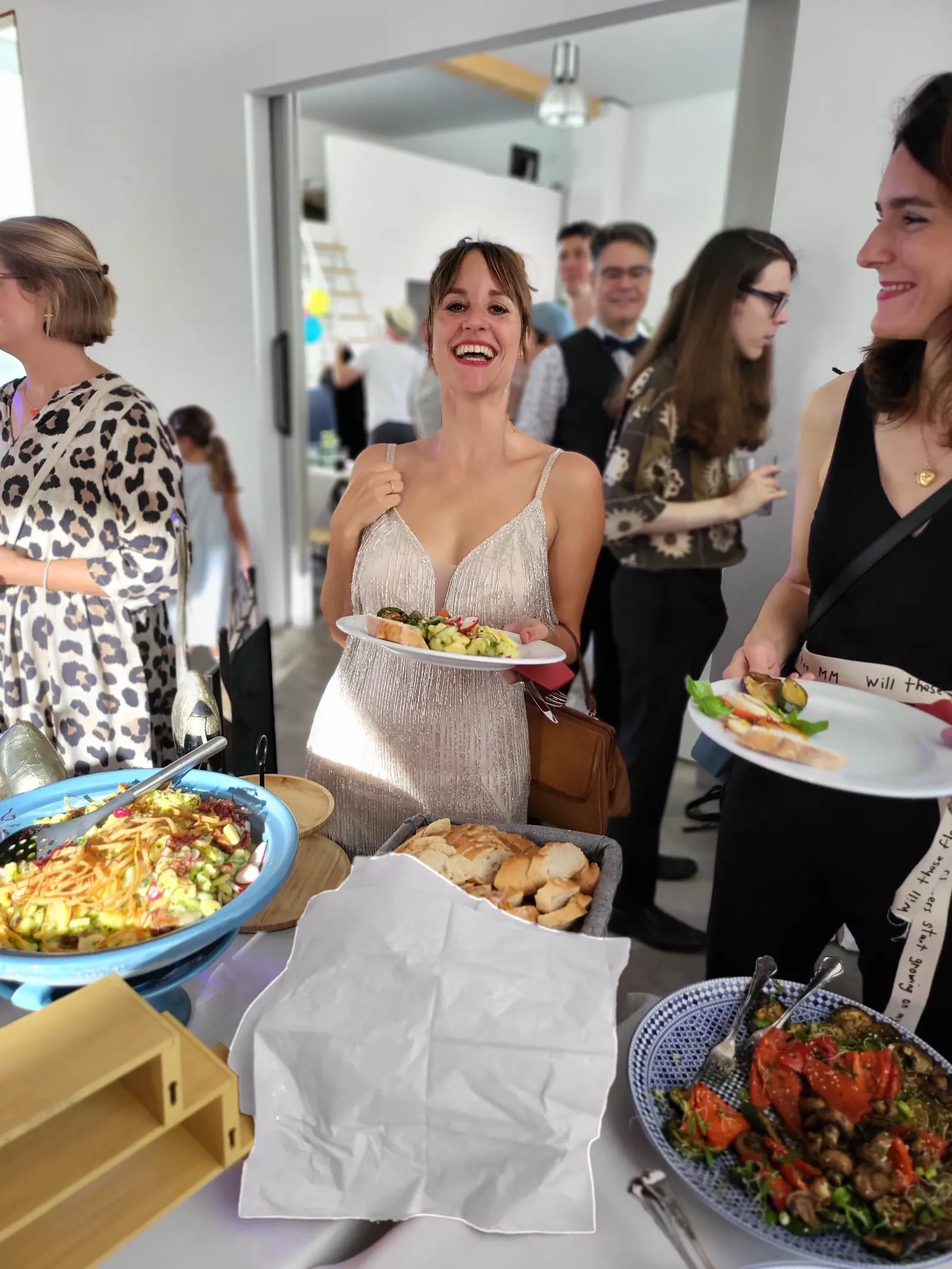Lachende Gäste mit gefüllten Tellern am Buffet einer privaten Feier